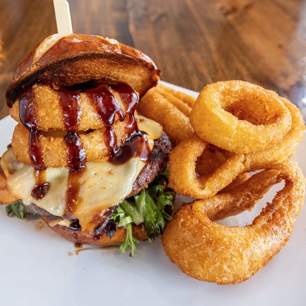 A WindMill Grille burger topped with onion rings, cheese, and BBQ sauce, served with onion rings.