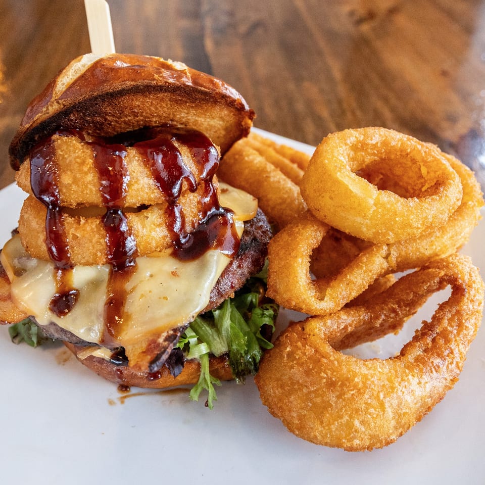 A WindMill Grille burger topped with onion rings, cheese, and BBQ sauce, served with onion rings.