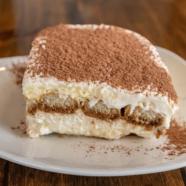 A close-up of a slice of tiramisu with layers of cream and ladyfingers, dusted with cocoa powder.