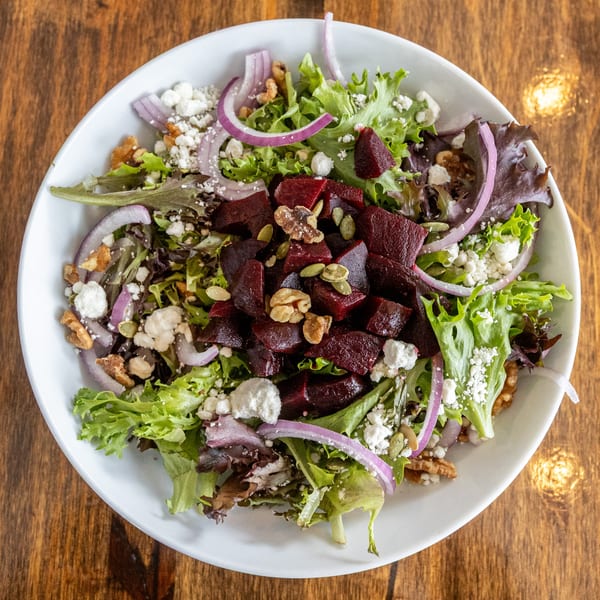 Overhead view of a fresh salad with mixed greens, beets, red onion, feta, walnuts, and pumpkin seeds.