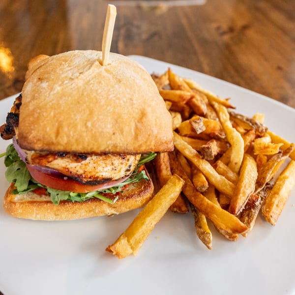 Grilled chicken sandwich with lettuce, tomato, and red onion, served with a side of fries.