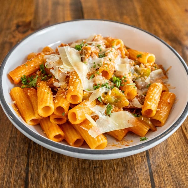 Rigatoni pasta with red sauce, green peppers, and parmesan cheese in a white bowl.