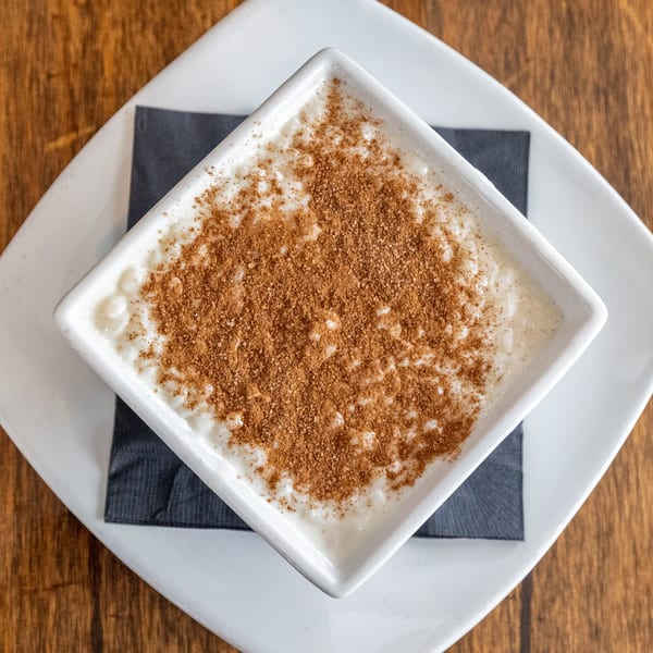 Creamy rice pudding topped with cinnamon and sugar, served in a white square bowl.