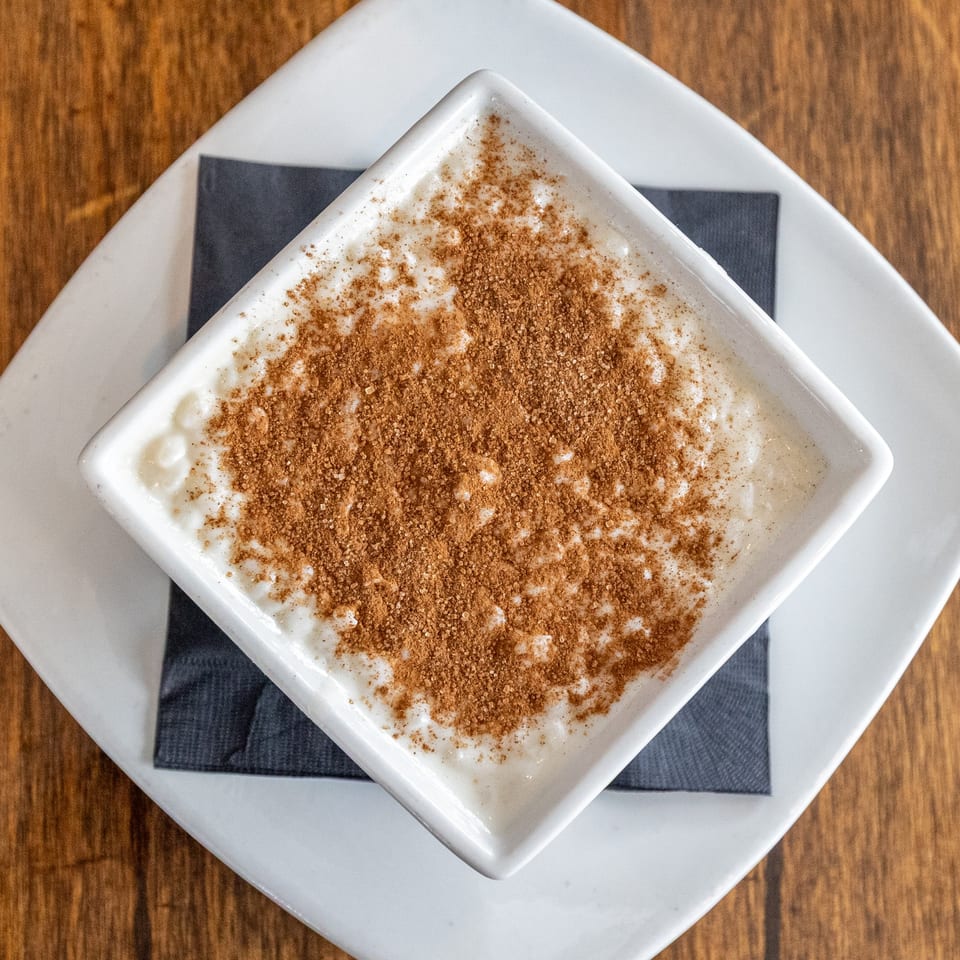Creamy rice pudding topped with cinnamon and sugar, served in a white square bowl.