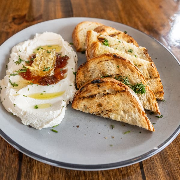 Whipped ricotta with honeycomb, fig jam, olive oil, and grilled bread on a gray plate.