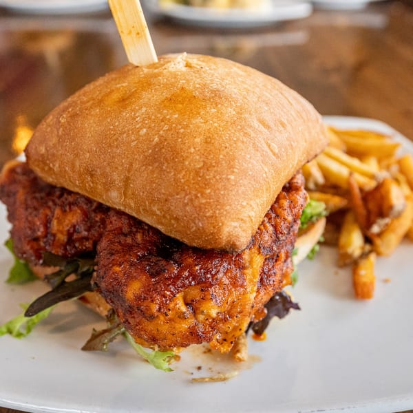 Spicy chicken sandwich with lettuce on a bun, served with a side of golden french fries.